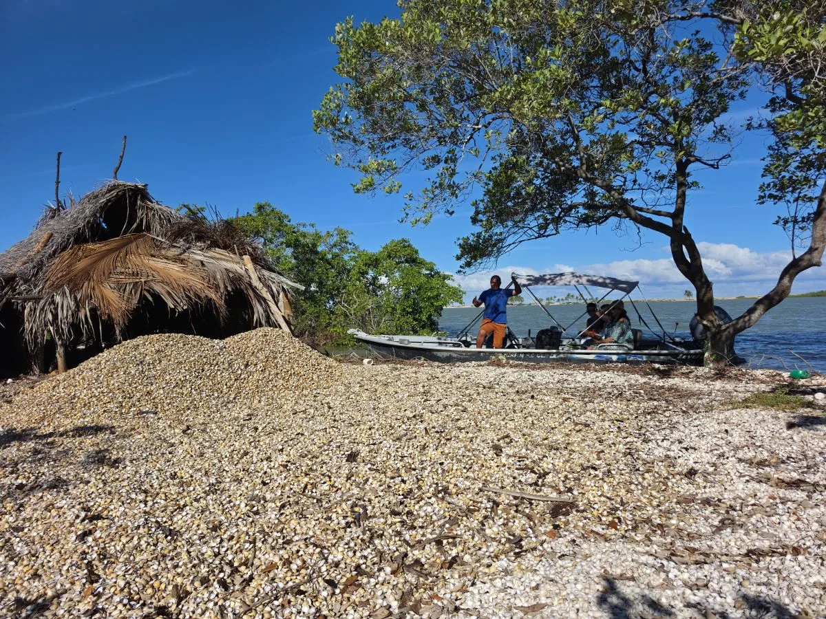 Cabana de palha e monte de conchas na praia, com barco atracado